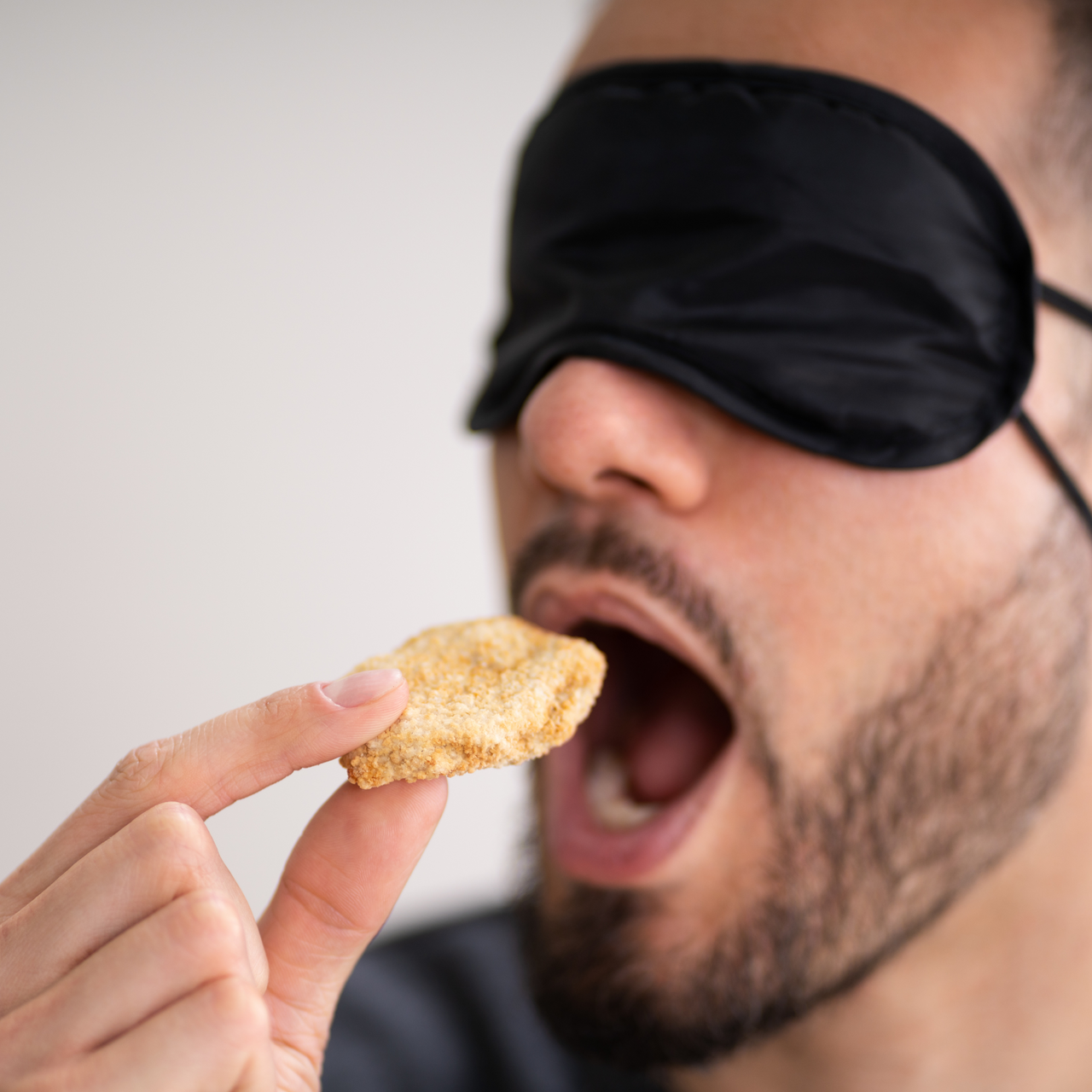Ein man mit Augenbinde ist einen Keks. Hier wird scheinbar die Achtsamkeit des Geschmackssinns auf die Probe gestellt. Eine Mögliche Anwendung für ein Teambuildingevent.